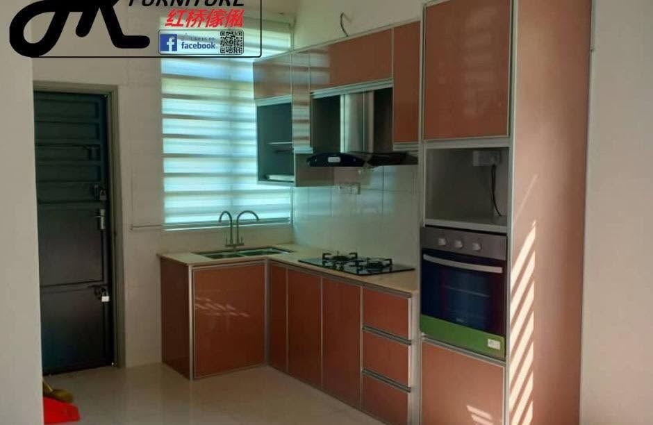 A compact L-shaped aluminium kitchen with copper-orange high-gloss doors, a stainless chimney hood, a glass-fronted wall unit and a built-in oven tower.