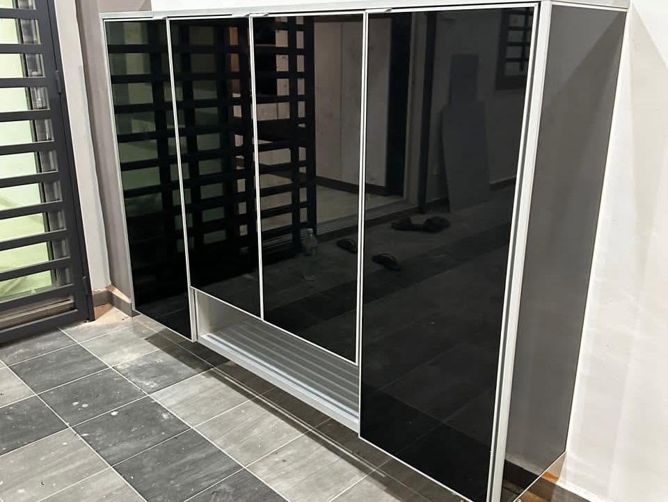 An aluminium-framed shoe cabinet with black glass sliding doors and a louvred base panel against a white wall on a tiled porch.