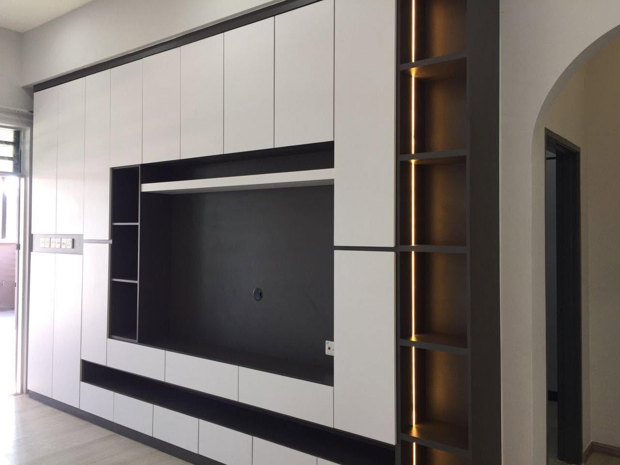 A full-height built-in television feature wall in matte white with dark charcoal shadow-gap trims, a recessed dark TV panel and a tall rack of open display niches lit by warm LED strips, in an empty room.